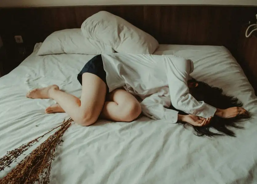 Liebeskummer-4.jpg Frau liegt seitlich zusammengerollt<br />
auf einem Bett mit weißer Bettwäsche
