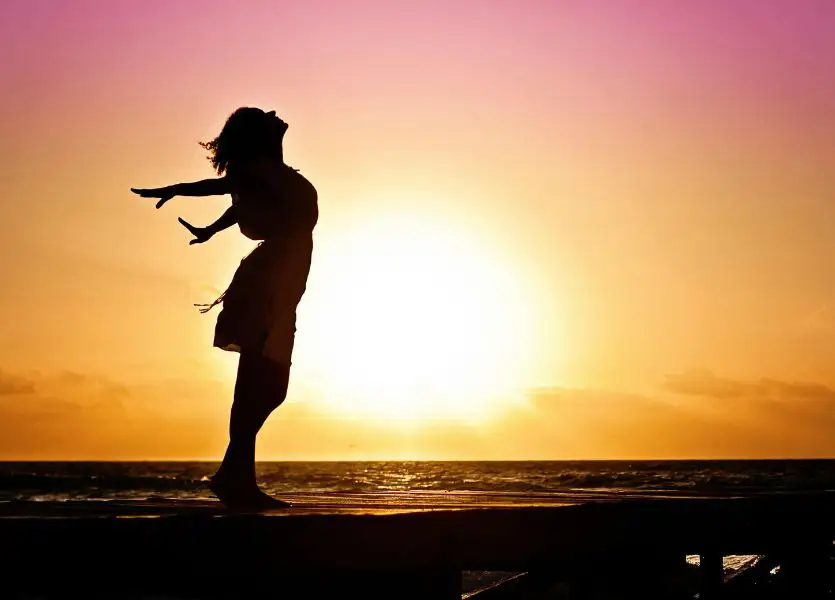 Liebeskummer-ade.jpg Frau steht mit ausgestreckten<br />
Armen am Meer vor<br />
Sonnenuntergang